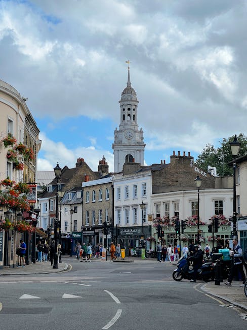 A quiet residential street in Tooting SW17 lined with row houses featuring white facades, bay windows, and brick detailing under a cloudy sky. The pavement on the right side is paved with concrete sla
